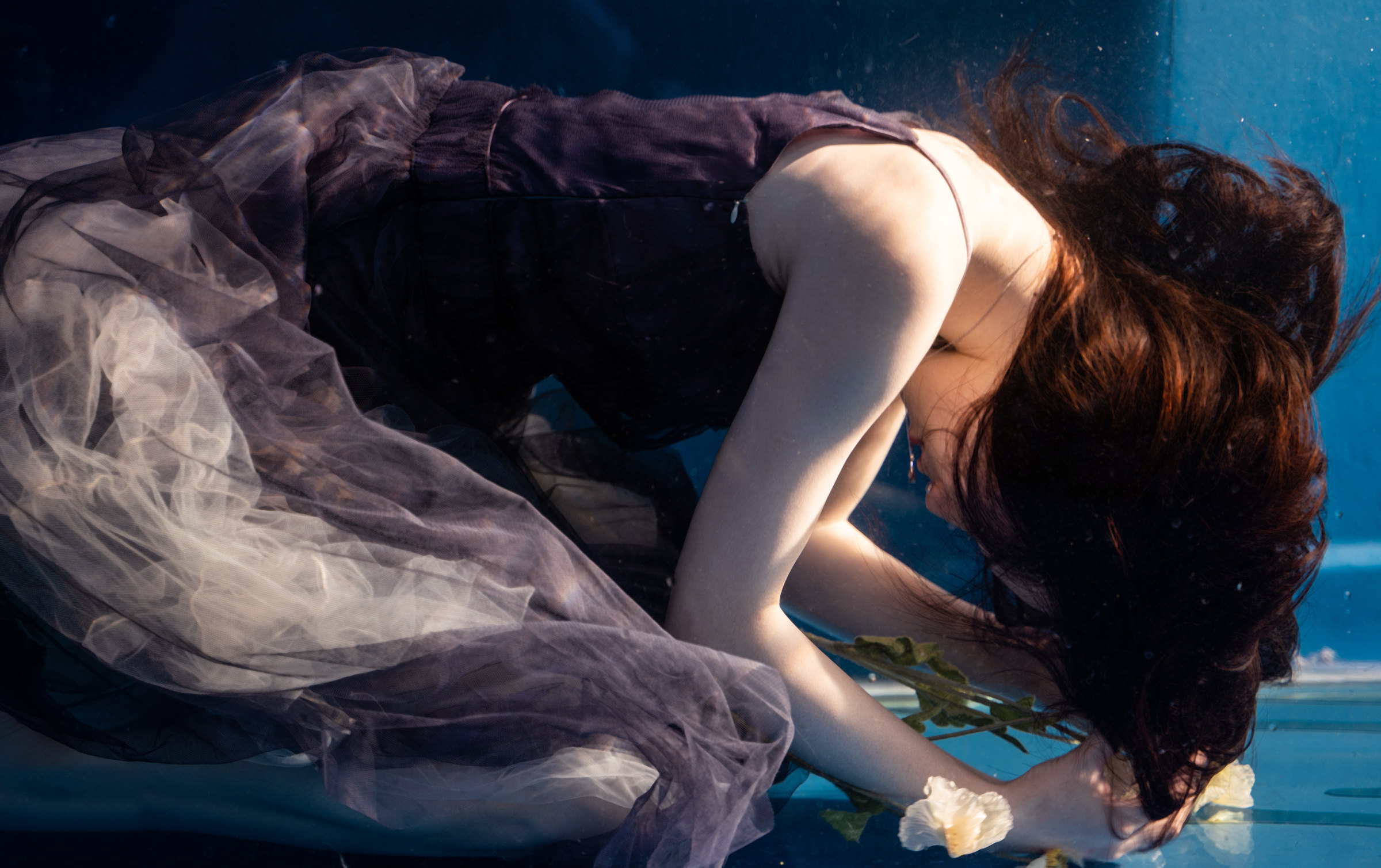 A woman folded forward beneath translucent fabric inside a tank