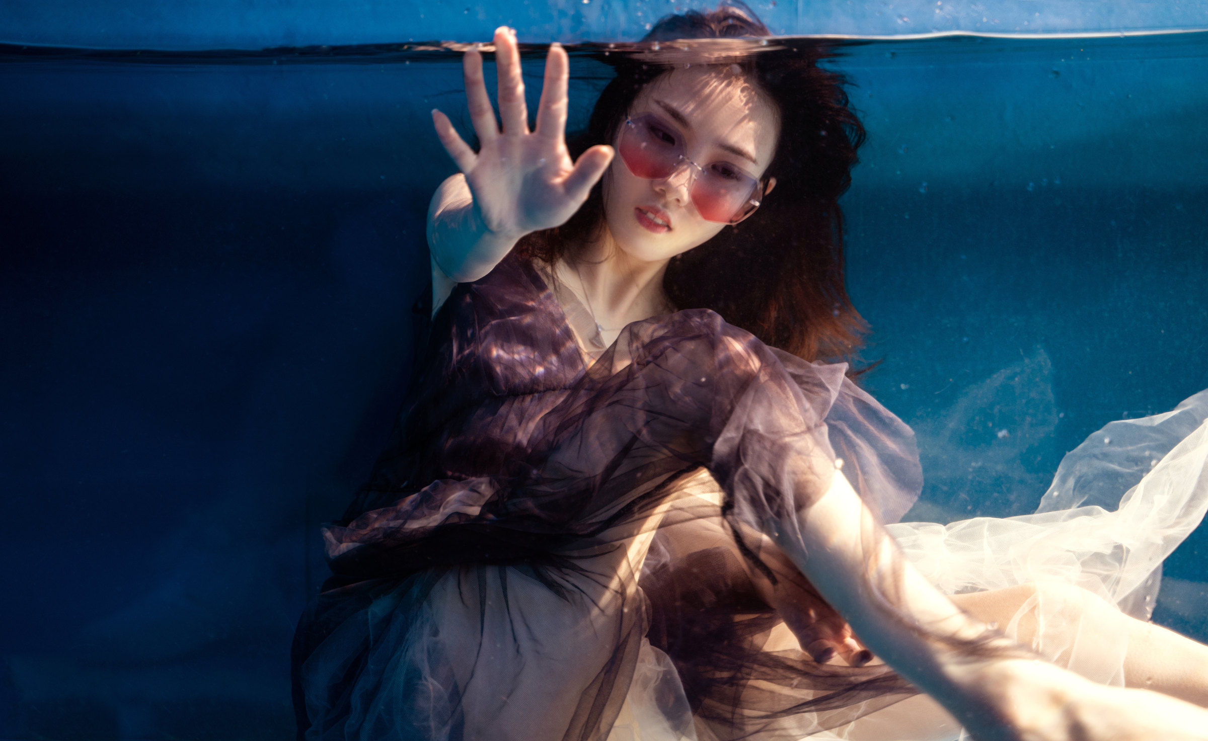 A woman reaches towards the glass from within the water
