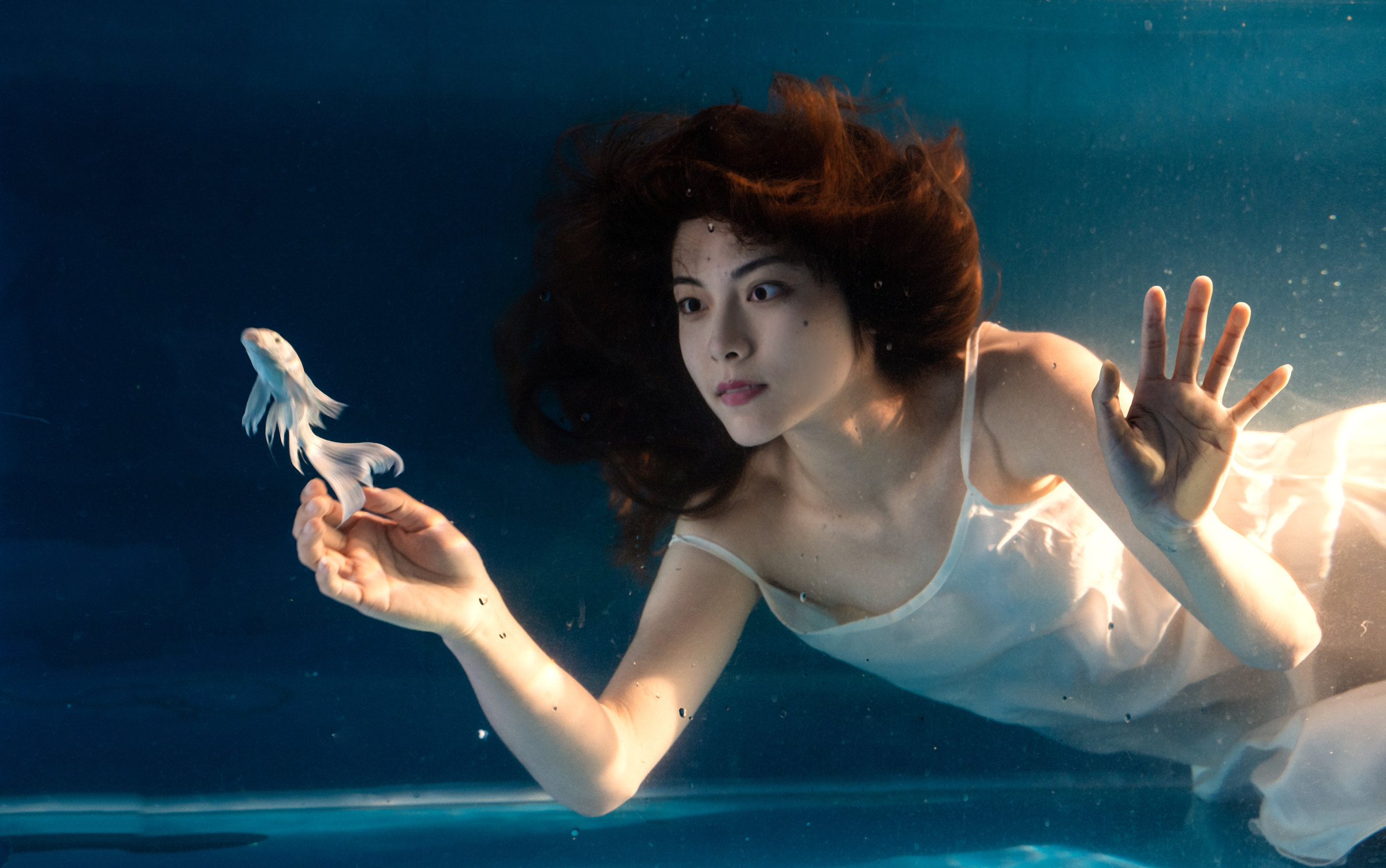 A woman in white looks towards a flowing white fish and raises an open hand
