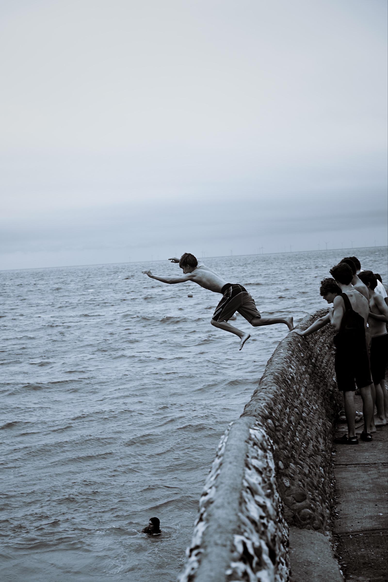 A young man leaves a seawall as a group watches