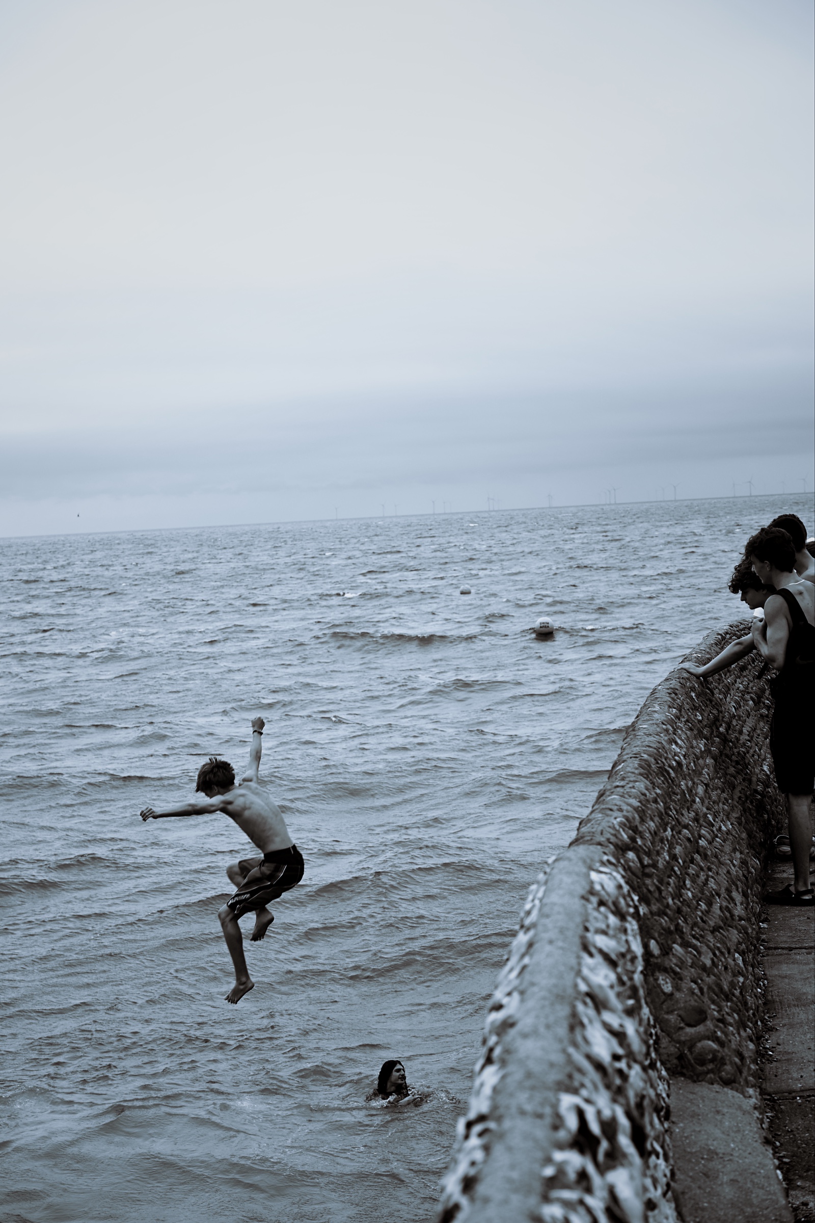 A young man descends beside the seawall while friends watch