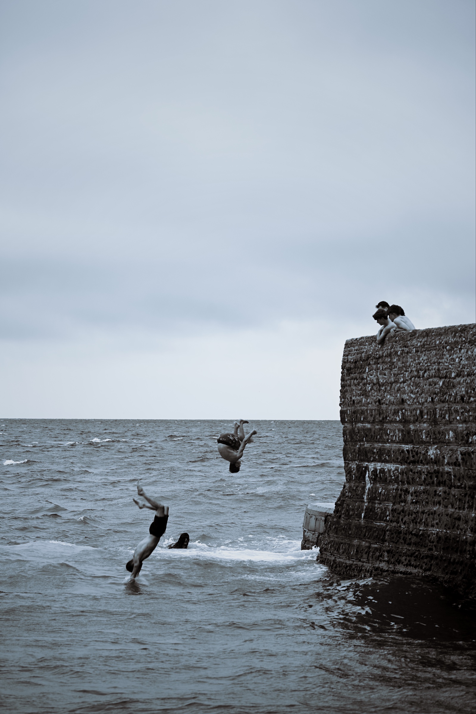 Two figures enter the sea at different stages while friends look on
