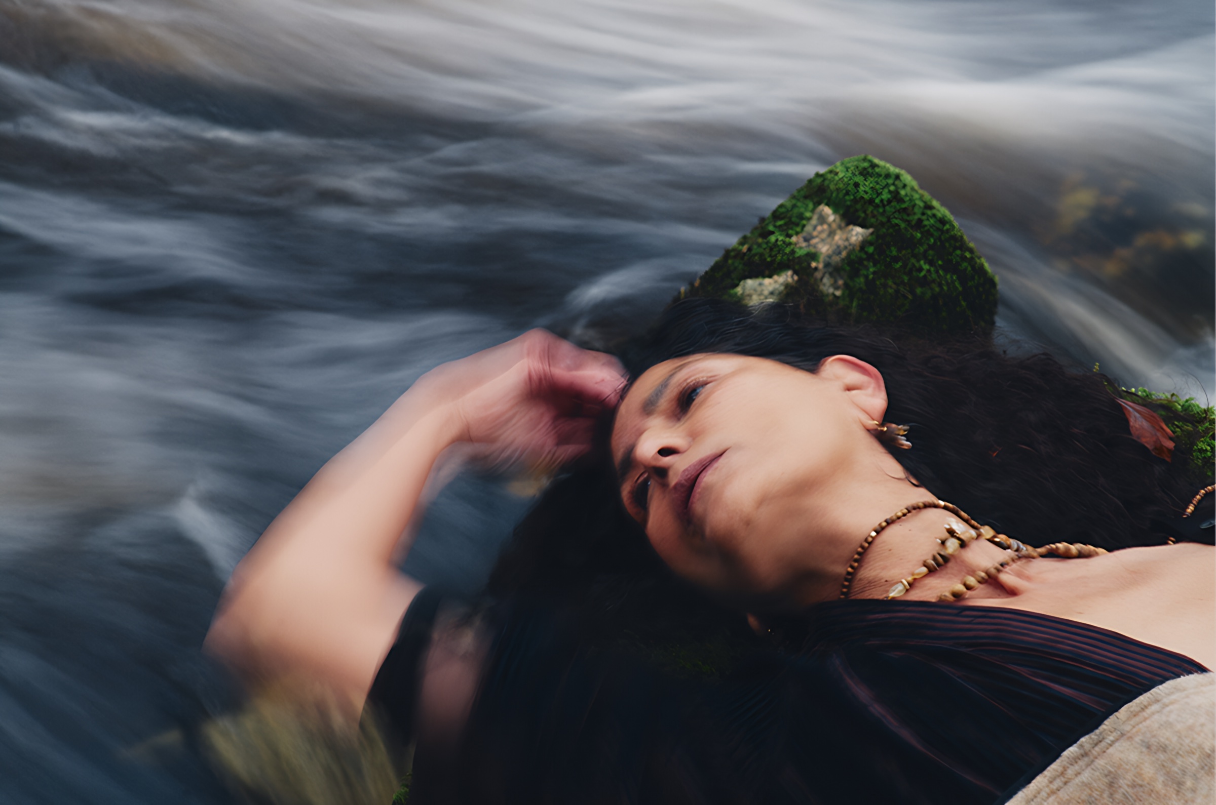 A figure lying beside a flowing stream with her head against a moss-covered stone