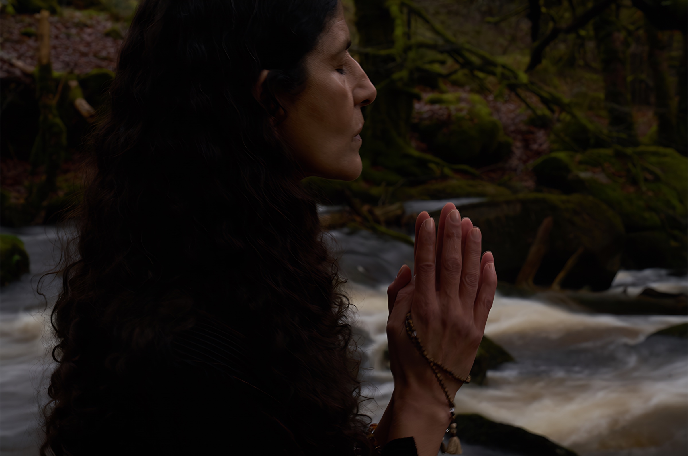 A profile portrait with hands joined beside a forest stream