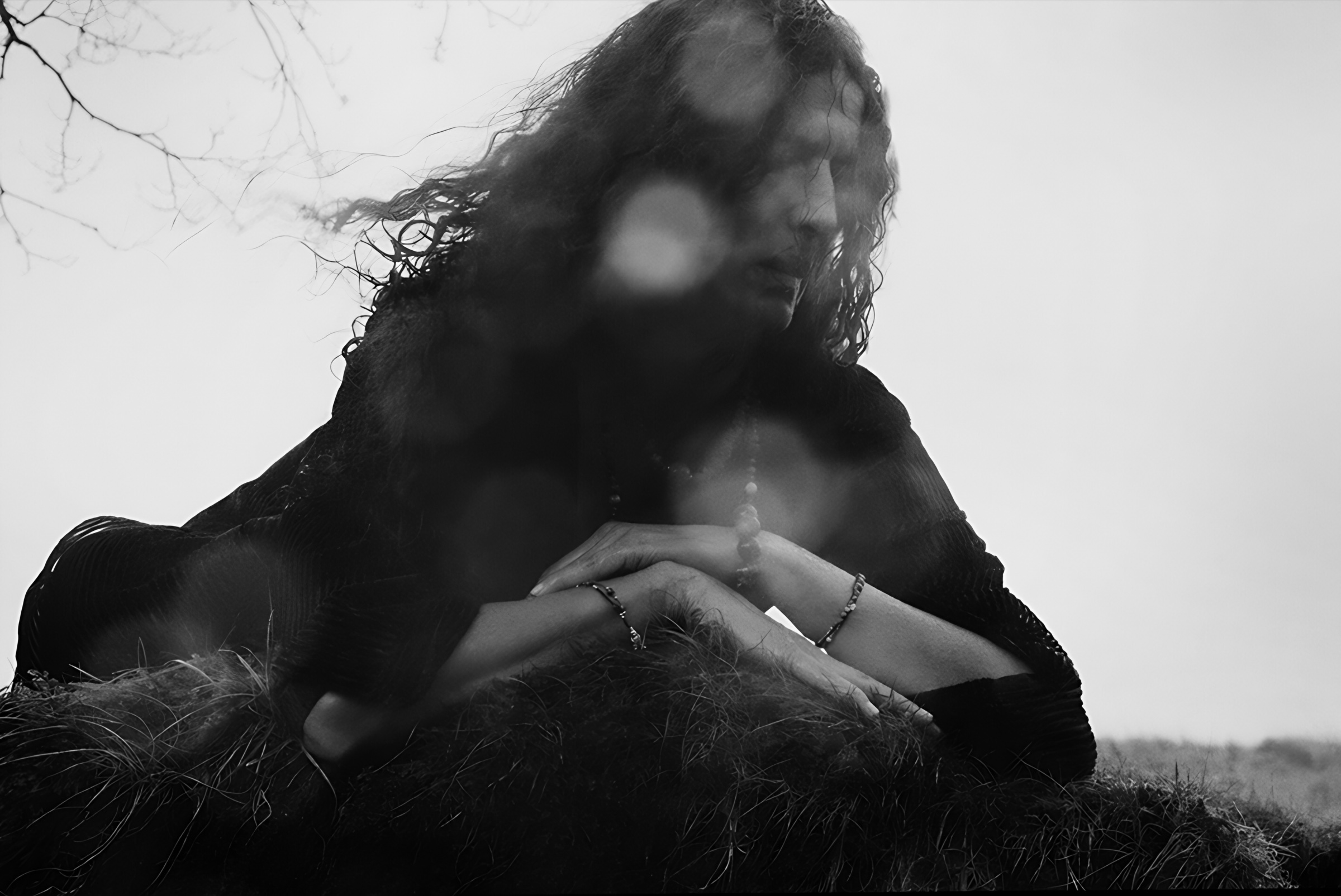 A black-and-white portrait with lowered gaze, seen through soft foreground branches